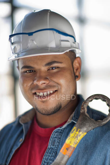 Jovem trabalhador da construção usando chapéu duro e segurando chave inglesa, sorrindo — Fotografia de Stock
