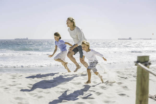Padre e hijos corriendo en la playa - foto de stock
