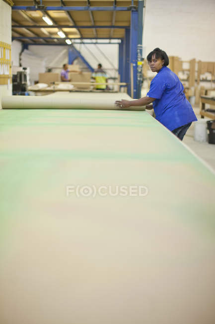 Tapicería femenina desenrollando la longitud del textil en el banco de trabajo - foto de stock