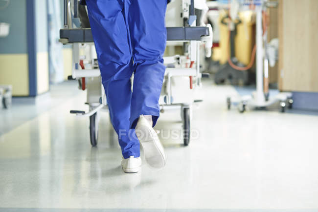 Piernas de médico corriendo con camilla a lo largo del pasillo del hospital - foto de stock