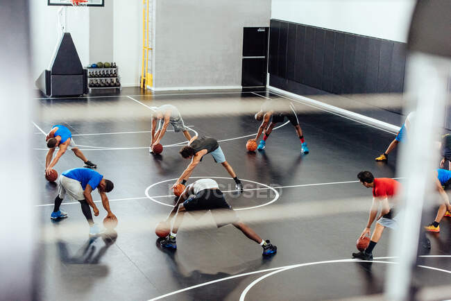Treinador masculino e jogadores de basquete se aquecendo esticando para a frente na quadra — Fotografia de Stock