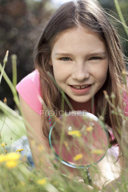 Portrait of girl lying in grass with magnifying glass — Stock Photo