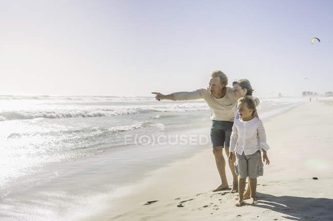 Отец и сыновья, указывающие на море на пляже — стоковое фото