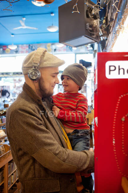 Padre sosteniendo joven hijo por teléfono público - foto de stock