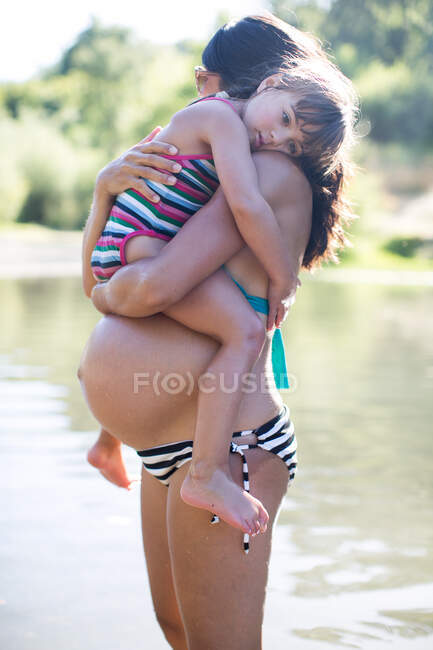 Embarazada madre holding hija joven - foto de stock