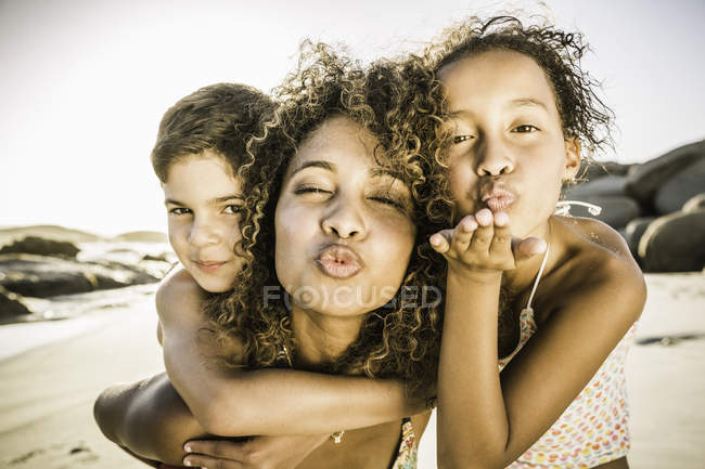 Mutter und Kinder blasen Küsse am Strand — Stockfoto