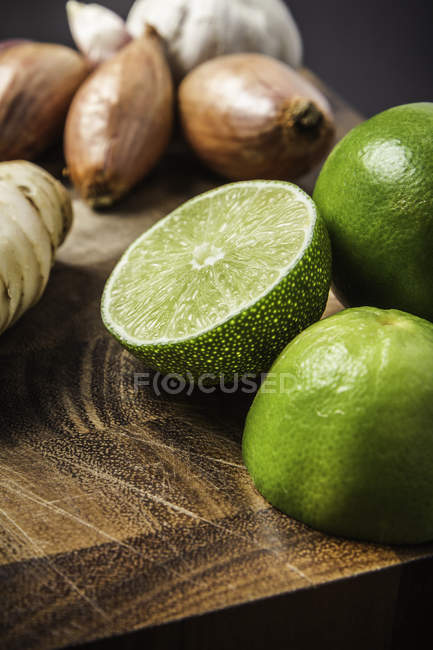 Limes entières et coupées en deux, ail, oignon et gingembre sur planche de bois — Photo de stock
