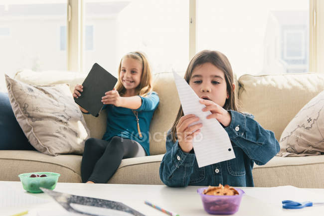 Las niñas en casa usando tableta digital, haciendo avión de papel - foto de stock