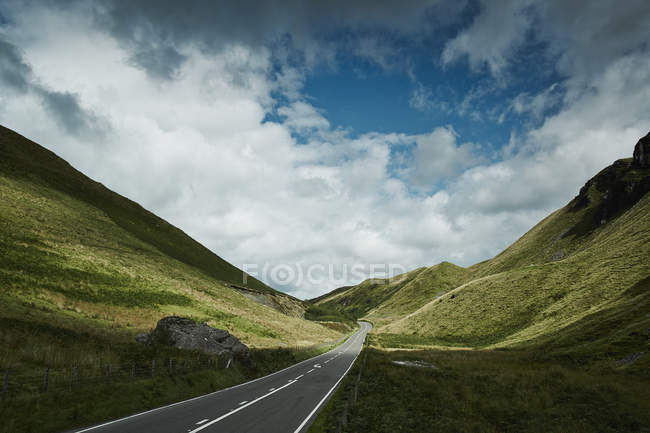 Уменьшающийся вид дороги, простирающейся между зелеными холмами солнечного света — стоковое фото