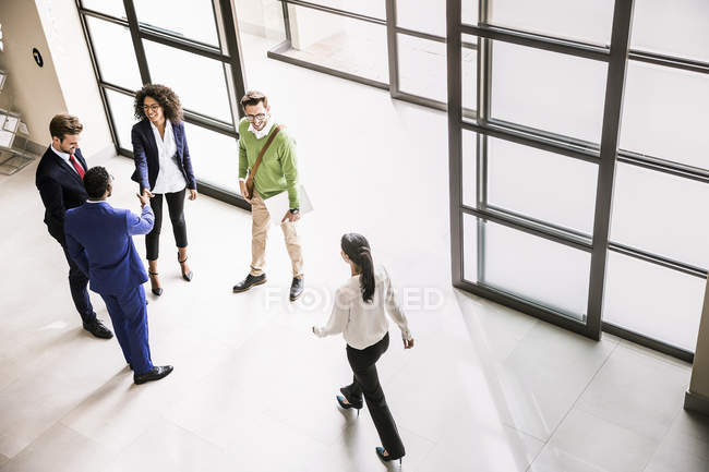 Vista de ángulo alto de hombres de negocios y mujeres saludándose en la entrada de la oficina - foto de stock