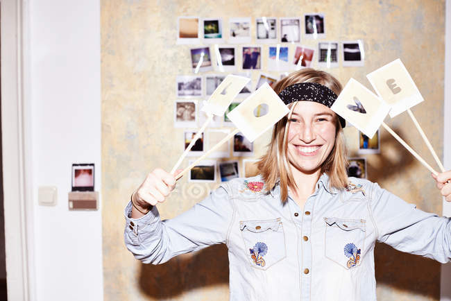 Young woman in front of photo wall holding up love sign — Stock Photo