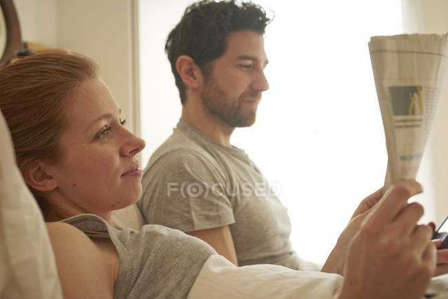Mediados de pareja adulta leyendo sábana ancha en la cama - foto de stock