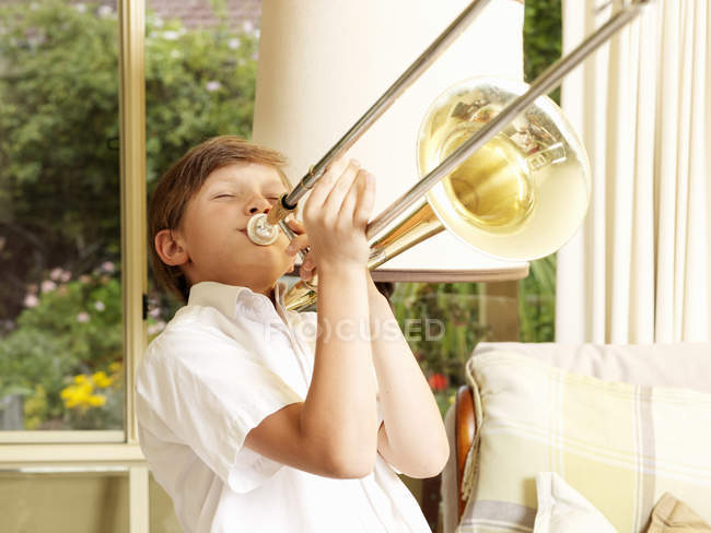 Rapaz a praticar trombone na sala de estar — Fotografia de Stock