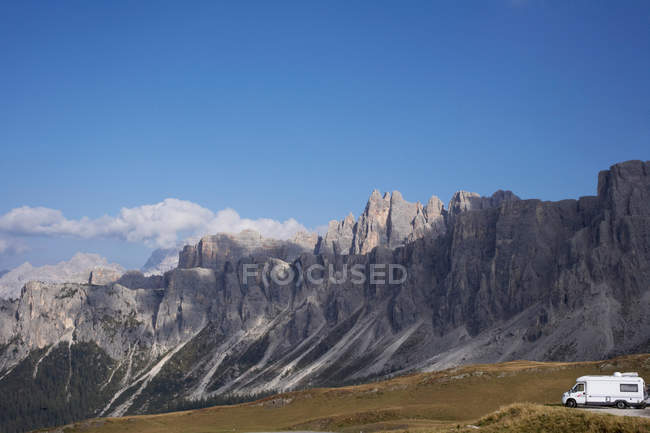 Camper van under rocky mountains with blue sky — Stock Photo