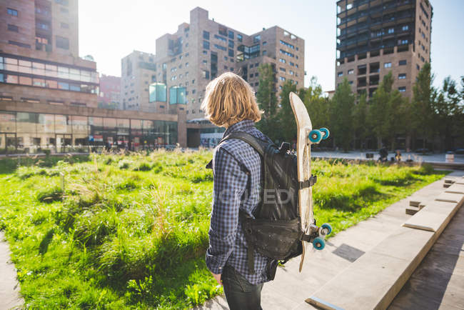 Joven skater urbano masculino llevando mochila con monopatín - foto de stock