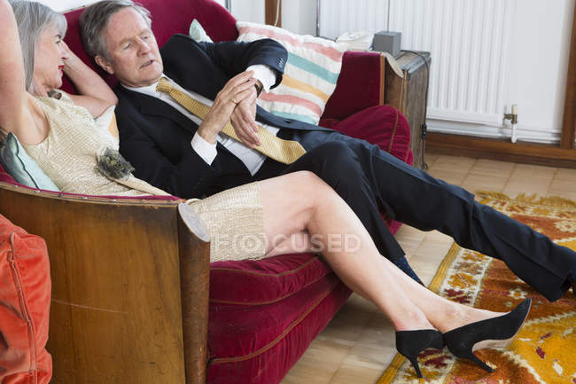 Couple habillé, assis sur le canapé et vérifiant l'heure — Photo de stock