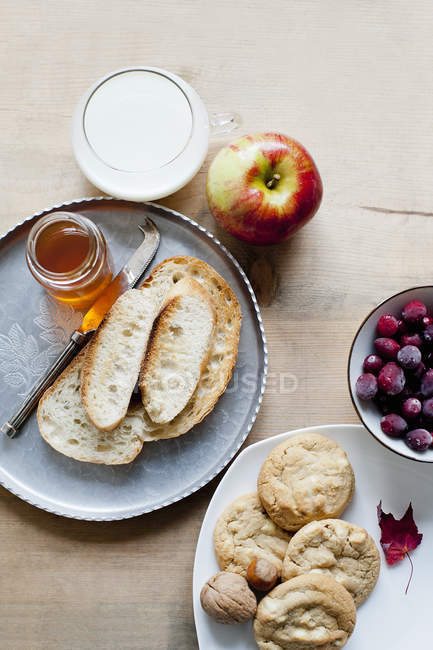 Ainda vida de baguete com mel, biscoitos, leite e frutos na mesa — Fotografia de Stock