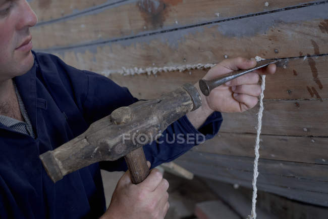 Homme martelant la ficelle dans le bateau dans l'atelier — Photo de stock