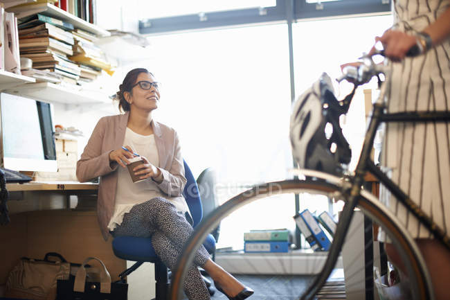 Mujer en la oficina con café charlando con su colega - foto de stock