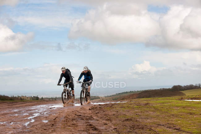 Couple riding mountain bikes through mud — Stock Photo