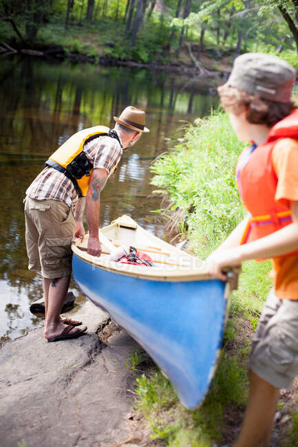 Padre e hijo empujando canoa en el río - foto de stock