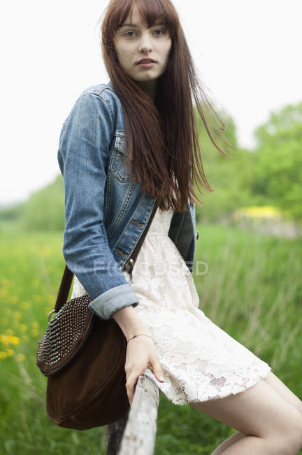 Portrait of young woman sitting on fence in field — Stock Photo