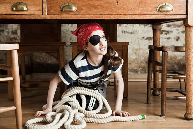 Jovencita vestida de pirata, debajo del escritorio - foto de stock