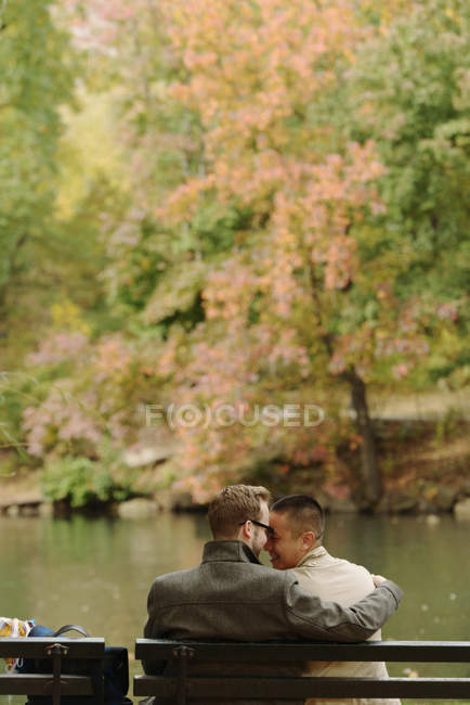Gay pareja abrazando en parque banco - foto de stock