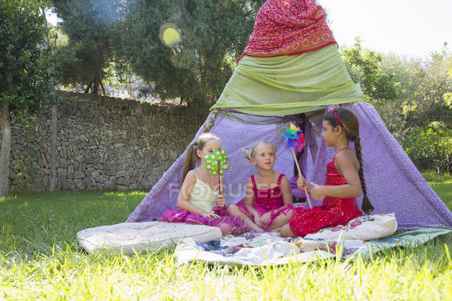 Three girls playing with pin wheels in front of teepee — Stock Photo