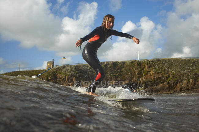 Joven surfista femenina cabalgando ola - foto de stock