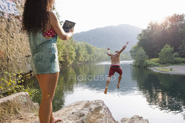 Mujer fotografiando novio saltando desde roca repisa, Hamburgo, Pensilvania, EE.UU. - foto de stock