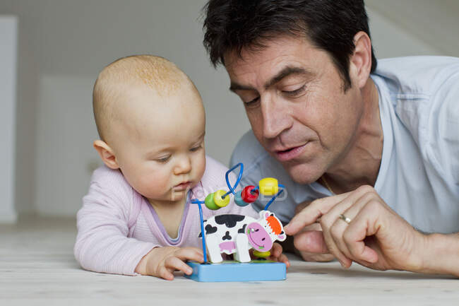 Mature man and baby daughter playing with toy cow — Stock Photo
