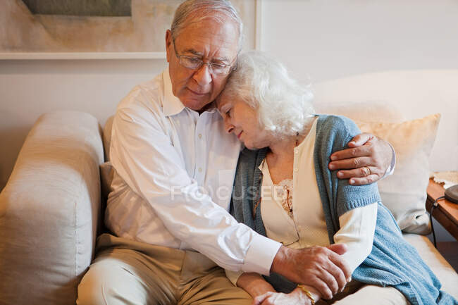 Старшая пара обнимается дома на диване — стоковое фото