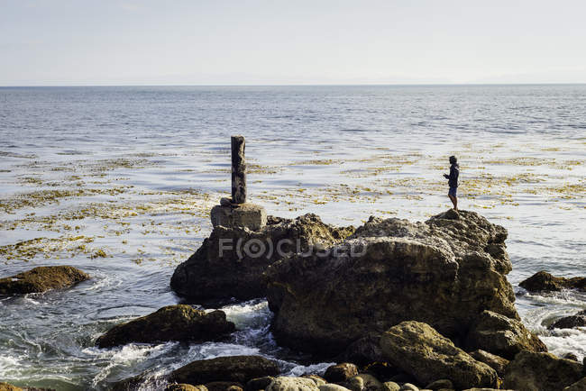 Homme mûr, debout sur des rochers par la mer, regardant la vue — Photo de stock