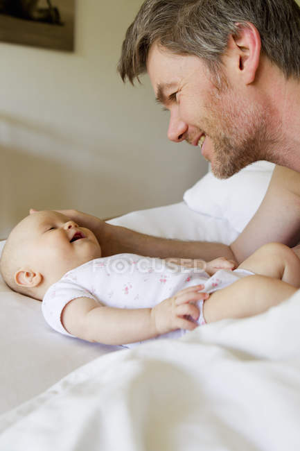 Padre sorridente alla bambina sul letto — Foto stock