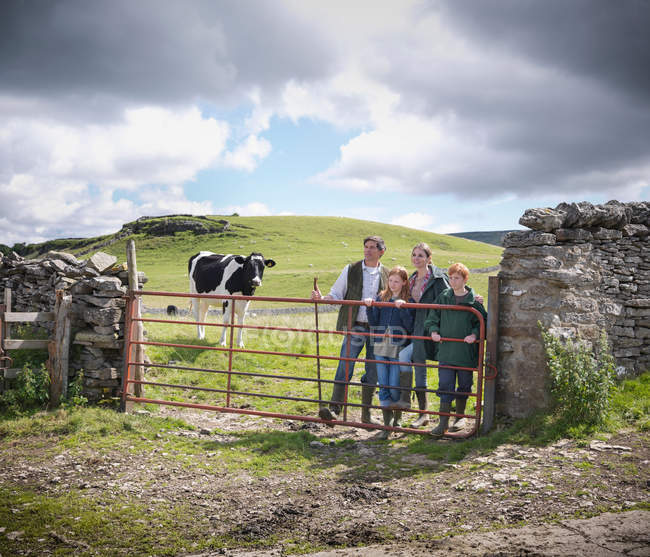 Ritratto di contadino e famiglia appoggiato al cancello con mucca in campo alle spalle — Foto stock