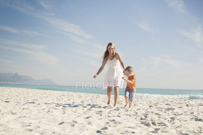 Menino correndo e puxando mãe na praia — Fotografia de Stock