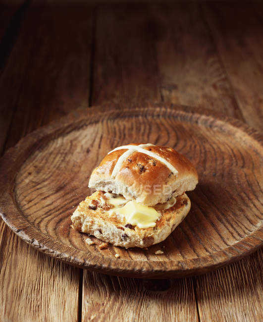 Buttered cross bun on vintage wooden plate — Stock Photo