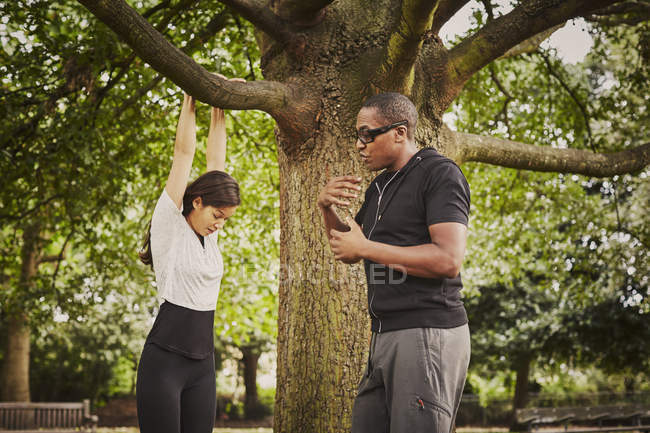 Entrenador personal instruyendo a la mujer en pull-ups utilizando la rama del árbol del parque - foto de stock