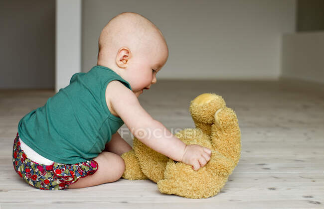 Baby girl playing with teddy bear on floor — Stock Photo