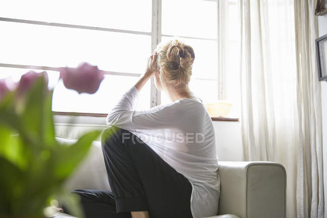 Женщина, сидящая перед окном и выглядывающая — стоковое фото