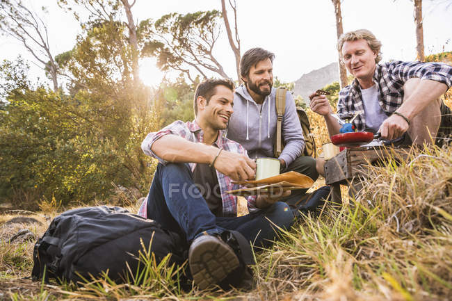 Tres hombres friendo el desayuno en la estufa de camping en el bosque, Deer Park, Ciudad del Cabo, Sudáfrica - foto de stock