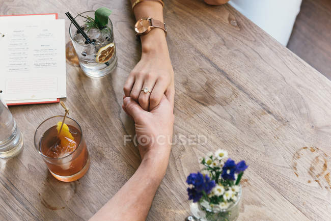 Immagine ritagliata della giovane coppia romantica che si tiene per mano sul tavolo del ristorante — Foto stock