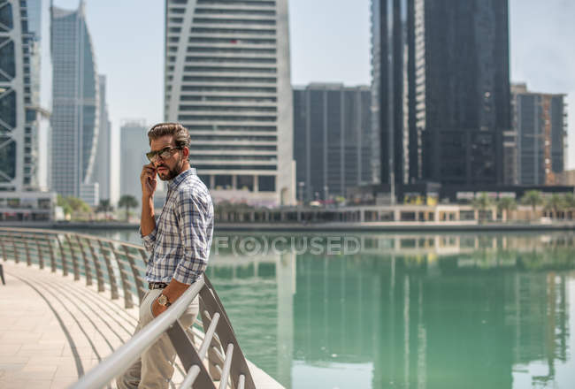 Young man leaning against waterfront railings talking on smartphone, Dubai, United Arab Emirates — Stock Photo