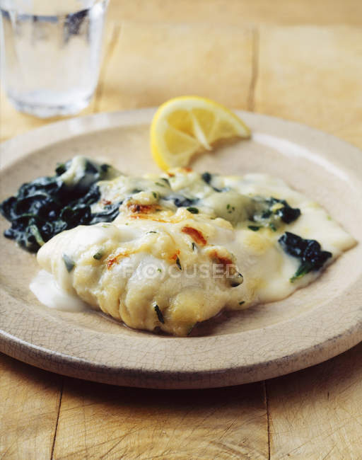 Cod in cream sauce with spinach and lemon slice — Stock Photo