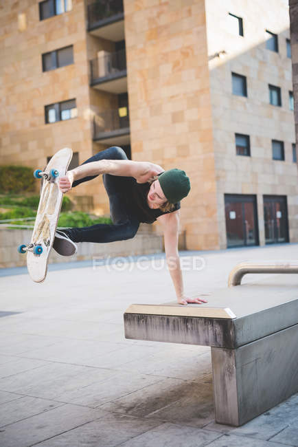 Young male skateboarder doing balance skateboard trick on urban concourse seat — Stock Photo