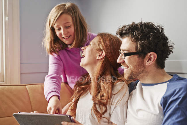 Батьки середнього віку і дочка на дивані дивляться на цифровий планшет — стокове фото