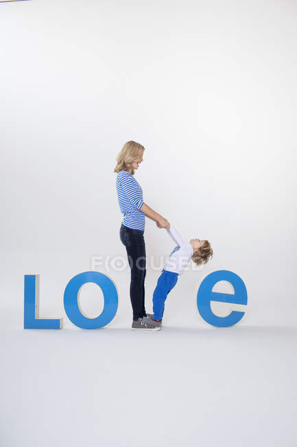 Mother and son holding hands, standing between three-dimensional letters, creating the word LOVE — Stock Photo