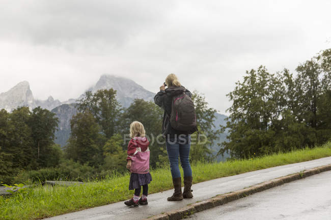 Rückansicht von Mutter-Tochter-Wanderern, die die Landschaft vom Straßenrand aus betrachten, Berchtesgaden, Watzmann, Bayern, Deutschland — Stockfoto