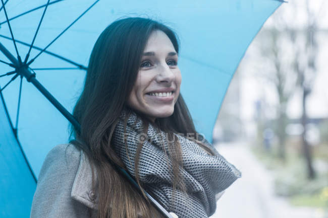 Portrait de jeune femme à l'extérieur, tenant un parapluie bleu — Photo de stock